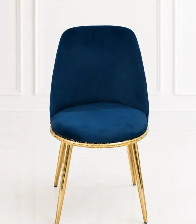 Luxury navy blue velvet dining chair with an ergonomic backrest, featuring a textured gold base rim and polished gold legs, set against a clean white paneled wall.