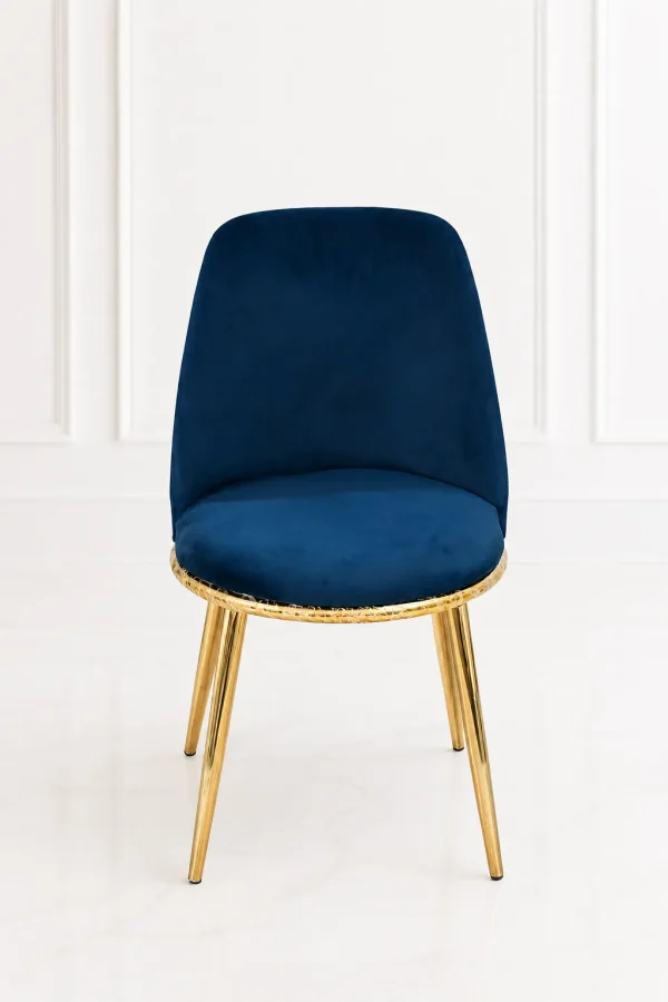 Luxury navy blue velvet dining chair with an ergonomic backrest, featuring a textured gold base rim and polished gold legs, set against a clean white paneled wall.
