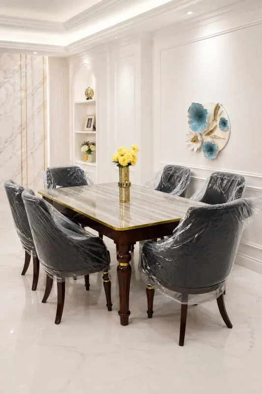 Luxury marble dining table set from featuring a polished gray marble rectangular table with gold trim, dark wood legs, and six matching dark leather tufted chairs in a bright white dining room.