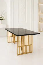 Luxury rectangular black marble dining table with natural gold veining, supported by open geometric vertical slatted gold legs in a bright white modern room.