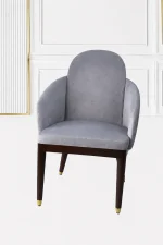 Luxury grey velvet armchair with an arched backrest, integrated sloped armrests, and dark wood legs with polished gold metallic feet caps.