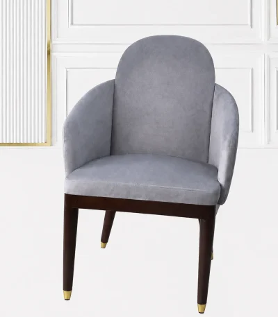 Luxury grey velvet armchair with an arched backrest, integrated sloped armrests, and dark wood legs with polished gold metallic feet caps.