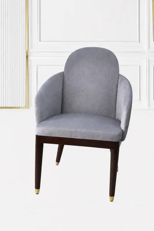 Luxury grey velvet armchair with an arched backrest, integrated sloped armrests, and dark wood legs with polished gold metallic feet caps.