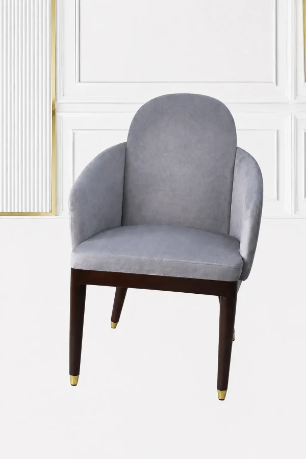 Luxury grey velvet armchair with an arched backrest, integrated sloped armrests, and dark wood legs with polished gold metallic feet caps.