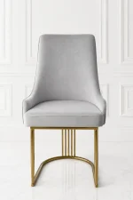 Front view of a luxury high-back light grey velvet dining chair supported by a polished gold stainless steel curved base with vertical slatted accents, against a white wall.