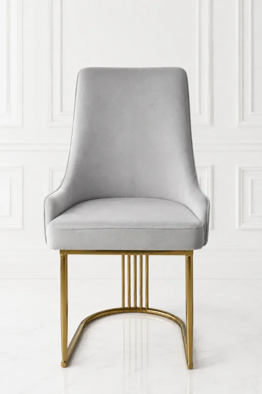 Front view of a luxury high-back light grey velvet dining chair supported by a polished gold stainless steel curved base with vertical slatted accents, against a white wall.