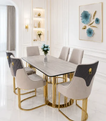 A luxury 6-seater dining set featuring a grey rectangular sintered stone tabletop on polished gold pillar legs, styled with six two-tone grey velvet chairs featuring diamond tufting and gold lion-head pulls in a bright, modern white dining room.