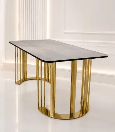 Rectangular grey wood dining table with rounded corners, supported by architectural curved pedestals made of vertical polished gold stainless steel slats, in a bright white modern room.