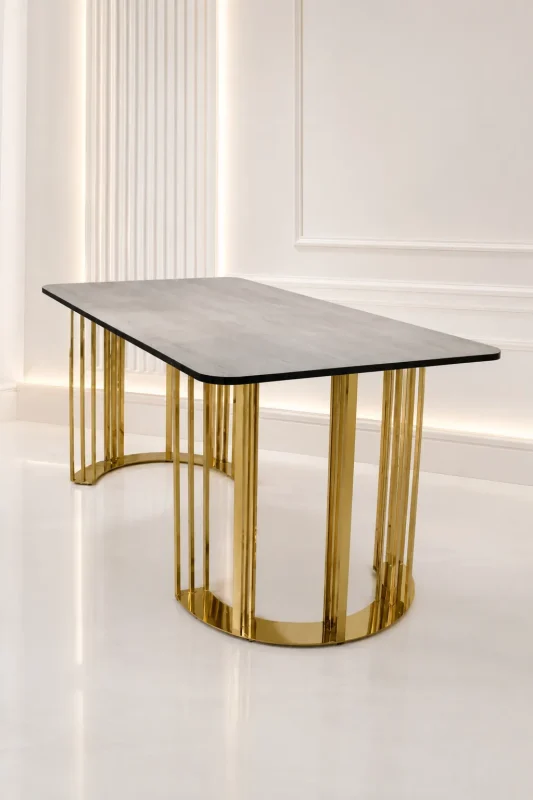 Rectangular grey wood dining table with rounded corners, supported by architectural curved pedestals made of vertical polished gold stainless steel slats, in a bright white modern room.
