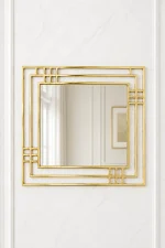 Square gold Art Deco wall mirror with a geometric multi-layered frame mounted on a minimalist white marble wall.