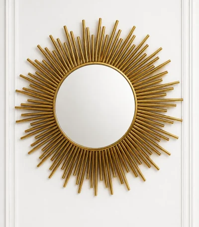Luxury gold sunburst wall mirror with a multi-layered starburst stainless steel frame centered on a white paneled wall.