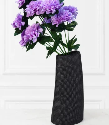 Tall black textured ceramic vase holding artificial purple flowers on a marble surface
