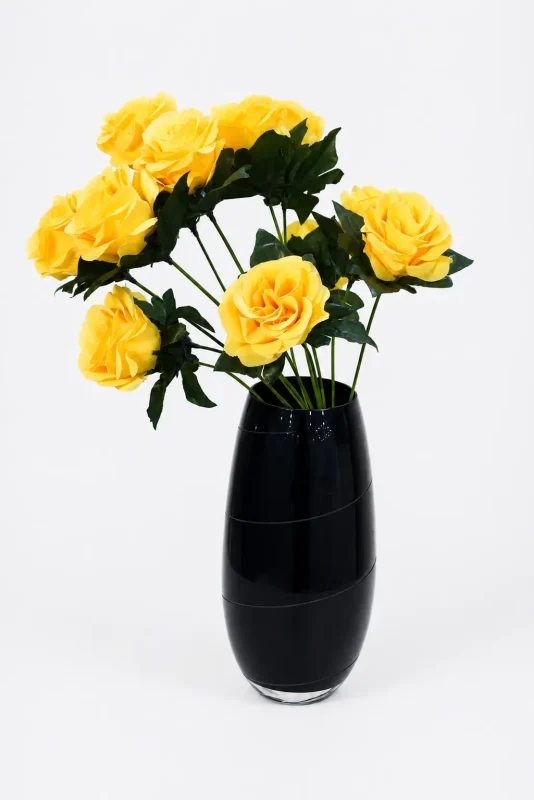 Tall black textured ceramic vase holding artificial purple flowers on a marble surface,