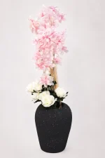 Speckled black vase with tall pink cherry blossoms and white roses on a white background