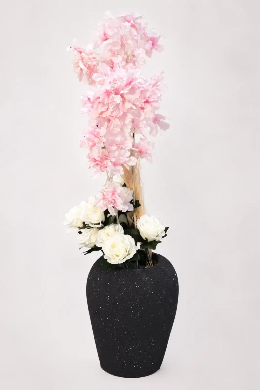 Speckled black vase with tall pink cherry blossoms and white roses on a white background