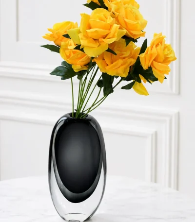Oval black and clear glass vase filled with artificial yellow roses on a marble table