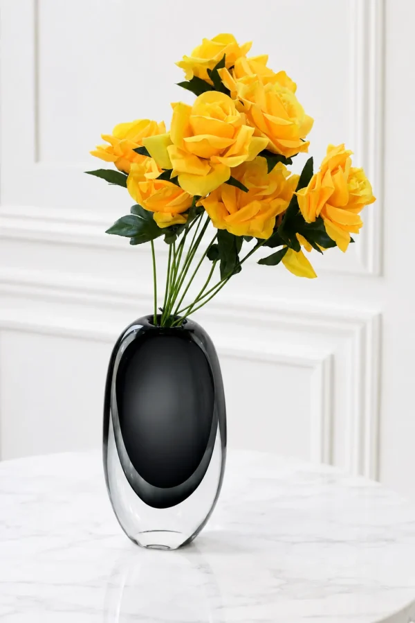 Oval black and clear glass vase filled with artificial yellow roses on a marble table