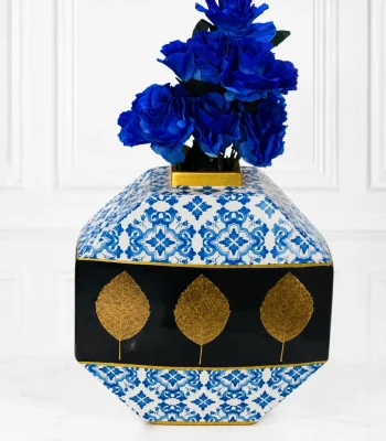 Geometric blue and white patterned vase with gold leaf accents holding royal blue roses on a marble surface
