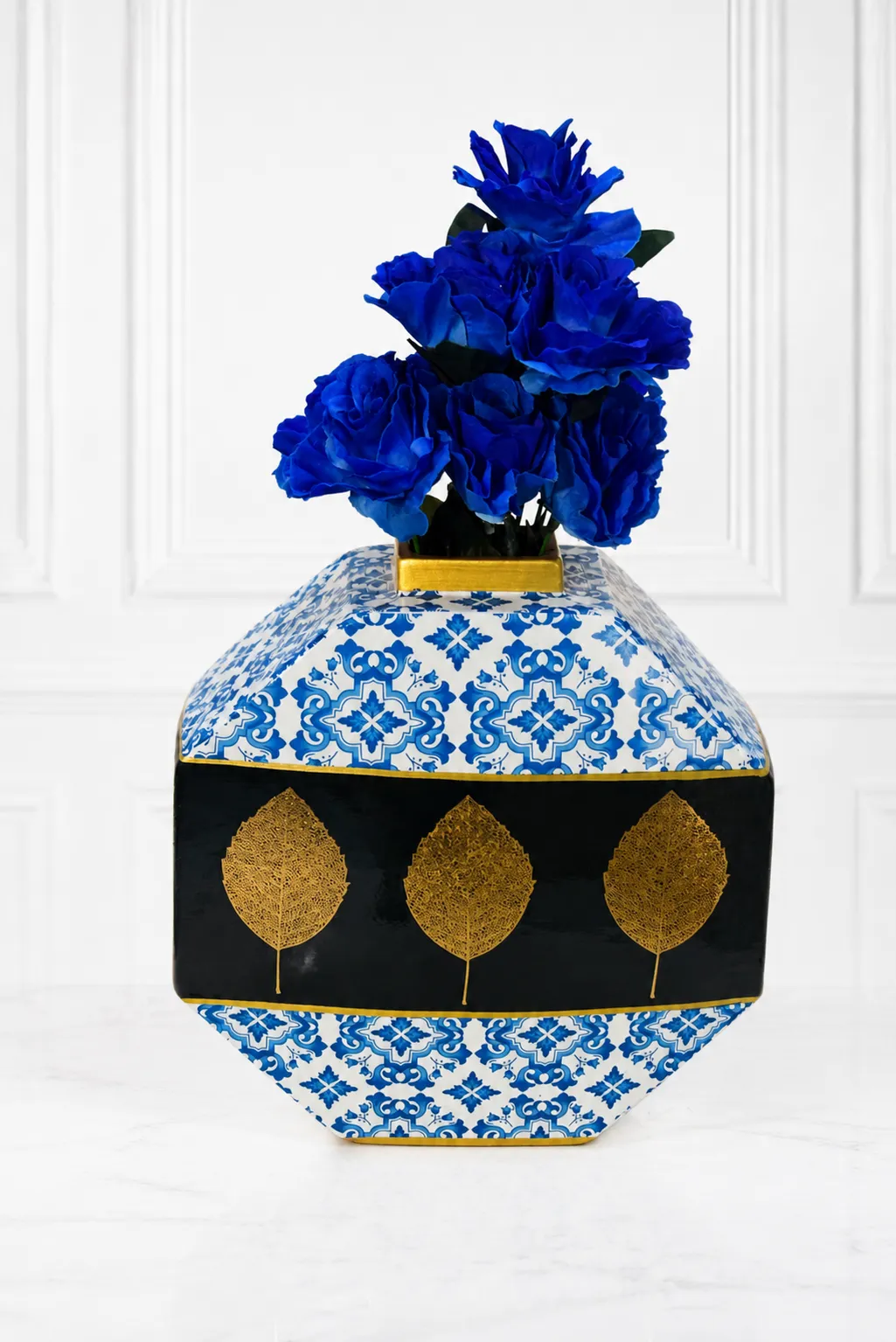 Luxury Octagonal Blue and White Ceramic Vase with Gold Leaf Accents and Faux Royal Blue Roses Geometric blue and white patterned vase with gold leaf accents holding royal blue roses on a marble surface