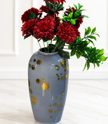 Alt-Text: Glossy grey ceramic vase with gold starburst details holding faux red flowers on a marble floor