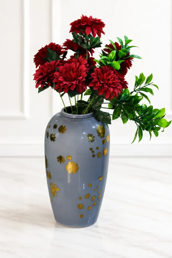 Alt-Text: Glossy grey ceramic vase with gold starburst details holding faux red flowers on a marble floor